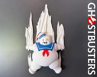 May include: A white Stay Puft Marshmallow Man wall decoration featuring a blue sailor collar, a red neckerchief, and a white hat with blue text. The figure is surrounded by white sculpted flames and the Ghostbusters logo is visible on the right.