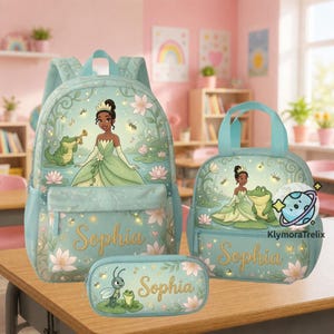 Puede incluir: Un conjunto de mochila, bolsa de almuerzo y estuche en color azul claro con una princesa en vestido verde, un caimán verde y un insecto. Cada pieza muestra el nombre Sophia en letras doradas, rodeado de flores de loto rosas y enredaderas.