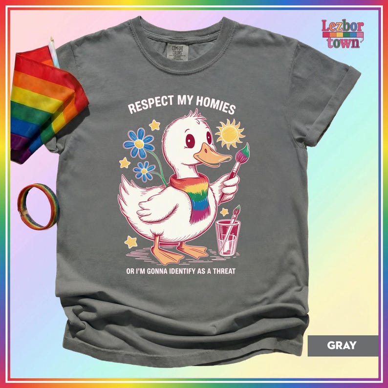 Puede incluir: Camiseta gris con un pato de dibujos animados con una bufanda arco&iacute;ris y un pincel. El texto "Respect My Homies" y "Or I'm Gonna Identify As A Threat" est&aacute; impreso. Una bandera y una pulsera arco&iacute;ris son visibles.