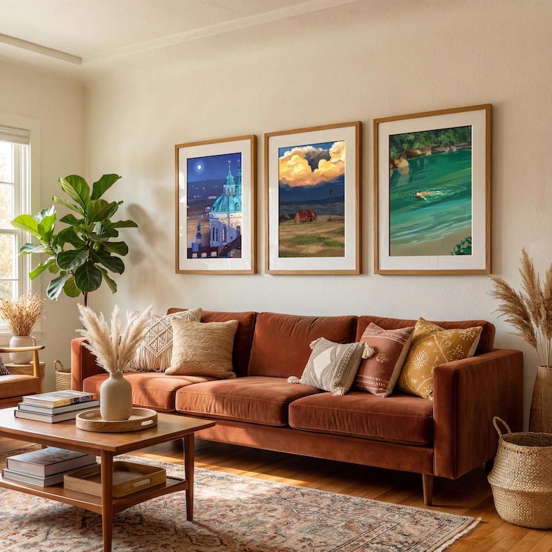 Puede incluir: Tres impresiones art&iacute;sticas enmarcadas cuelgan sobre un sof&aacute; color &oacute;xido. Las impresiones representan paisajes con una escena nocturna, una puesta de sol y una nadadora en un lago. Cojines decorativos y una mesa de centro de madera completan la sala de estar.