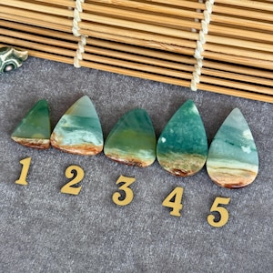May include: Five polished gemstone cabochons in shades of green, blue, and brown, arranged in a row. Each stone has a unique pattern, with a mix of colors and textures. The numbers 1 through 5 are placed below the stones.
