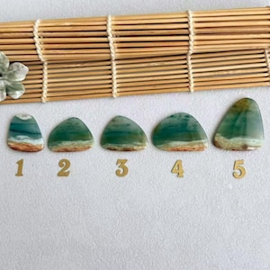 May include: Five polished, teardrop-shaped gemstones arranged in a row, each featuring a gradient of teal, green, and tan colors resembling a landscape. Each stone is labeled with a gold-colored number from one to five underneath it.