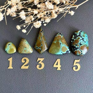 Puede incluir: Cinco piedras preciosas de turquesa pulida dispuestas en fila, cada una etiquetada con un número de color dorado del uno al cinco. Las piedras muestran formas variadas, incluyendo ovaladas y triangulares, con patrones de matriz marrones y negros.