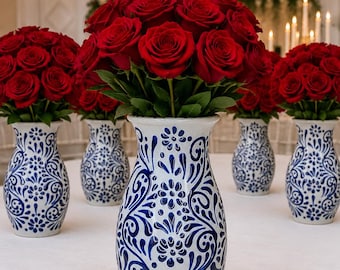 May include: A collection of white ceramic vases featuring intricate blue floral and scroll patterns, each filled with a dense arrangement of vibrant red roses. The vases are arranged in a group, showcasing a consistent design and color palette.