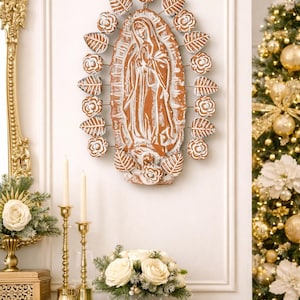Może przedstawiać: Rustykalny, terakotowy obraz ścienny przedstawiający postać religijną, otoczony białymi akcentami kwiatowymi i liściastymi. Obraz umieszczony jest na białej ścianie, z choinką i elementami dekoracyjnymi w tle. Ogólnym motywem jest wystrój religijny.