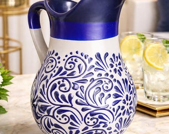 May include: A ceramic pitcher with a white base and a navy blue top and handle. The pitcher features a blue floral design and is suitable for serving beverages. The pitcher is approximately 10 inches tall.