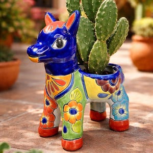 May include: A colorful ceramic donkey planter with a cactus inside. The donkey is painted with blue, yellow, green, orange, and red floral patterns. The planter is a decorative item for home or garden decor.