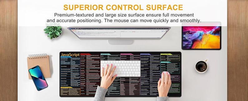 May include: A black and multi-colored JavaScript mouse pad with a white keyboard and a pink mouse. The mouse pad has a large surface area and includes the text "SUPERIOR CONTROL SURFACE". A smartphone, tablet, and coffee cup are also visible.