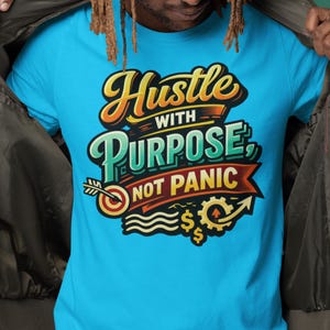 Könnte beinhalten: Hellblaues T-Shirt mit dem Text "Hustle with Purpose, Not Panic" in einem farbenfrohen, stilisierten Design. Die Grafik enthält eine Zielscheibe, einen Pfeil, Dollarzeichen und ein Zahnrad, alles im Vintage-Stil.