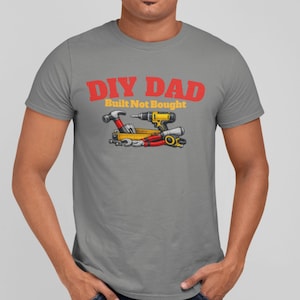 May include: A gray t-shirt with the text "DIY DAD Built Not Bought" in red and yellow. The shirt features a graphic of tools, including a hammer, drill, and measuring tape, perfect for a DIY enthusiast.