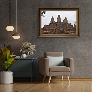 Peut inclure: Une photographie encadrée d'un temple à trois tours, sur fond de ciel nuageux. Le cadre est doré et l'image est montée sur un mur texturé gris. Le texte "PRE RUP" est visible dans le coin inférieur gauche.