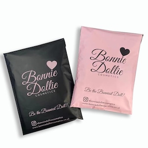 Könnte beinhalten: Zwei Kosmetik-Versandtaschen, eine schwarze und eine rosa. Jede Tasche trägt den Text "Bonnie Dollie Cosmetics" mit einem Herzsymbol und dem Satz "Be the Bonniest Doll!" Social-Media-Handles sind ebenfalls sichtbar.