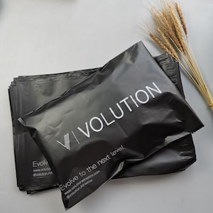 May include: A stack of black poly mailer shipping bags with the word "VOLUTION" in white. The text "Evolve to the next level" and website information are also printed on the bags. A bundle of wheat stalks is in the background.