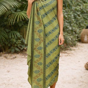 Könnte beinhalten: Ein grünes Sarong mit blau-braunen Mustern. Das Sarong ist um den Körper gewickelt und bildet ein schulterfreies Kleid. Der Stoff ist leicht und scheint aus einem weichen Material zu sein.