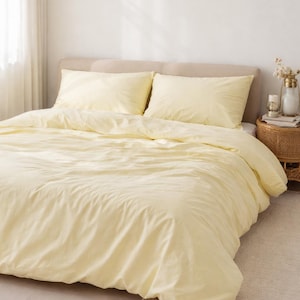 Könnte beinhalten: Ein Bett mit einer hellgelben Bettdecke und zwei passenden Kissenbezügen. Die Bettwäsche ist auf einem beigefarbenen Bettrahmen drapiert. Ein kleiner Teppich und ein Nachttisch mit dekorativen Gegenständen vervollständigen die Szene.