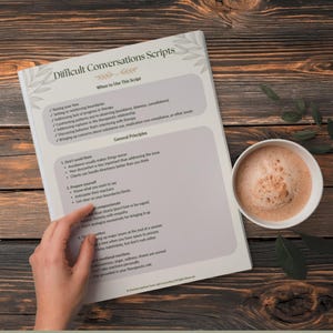 May include: A printed script titled "Difficult Conversations Scripts" with text on a wooden surface. A cup of coffee sits next to the script. The script includes sections on when to use it and general principles.