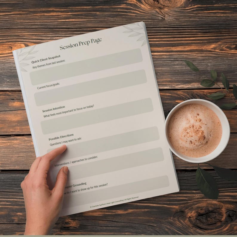 Może przedstawiać: Notatnik "Session Prep Page" z białą okładką i szarym tekstem, obok białego kubka kawy. Notatnik zawiera podpowiedzi dotyczące przeglądu klienta, skupienia, intencji i wskaz&oacute;wek. Tło to ciemna drewniana powierzchnia.