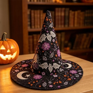 Könnte beinhalten: Ein schwarzer Hexenhut mit aufwendigen Stickereien von weißen Fledermäusen, violetten Blumen, orangen Beeren und Mondsicheln. Der kegelförmige Hut hat eine breite, flache Krempe und ist mit detaillierten Blattmustern auf dem Stoff verziert.