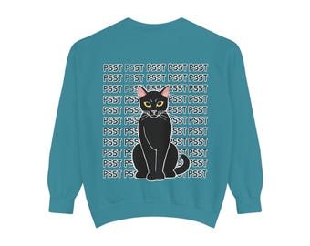 May include: Teal sweatshirt featuring a black cat illustration with yellow eyes. The cat is centered on the front, with the word "PSST" repeated in a pattern across the background. A casual, comfortable garment.