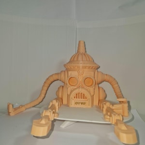 Könnte beinhalten: Ein hellorangefarbenes 3D-gedrucktes Roboterspielzeug mit einem gewölbten Kopf, zwei großen kreisförmigen Augen und dem Wort "OTTO" auf der Brust. Es hat zwei flexible Arme und zwei gegliederte Beine.