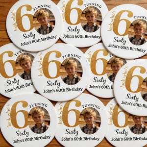 以下が含まれることがあります： 金色の数字60と「Turning Sixty」と「John's 60th Birthday」の文字が入った、白い丸いコースターのコレクション。各コースターには少年の写真が写っています。