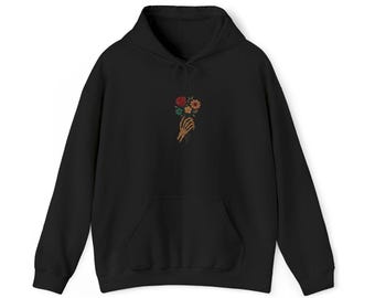 May include: Black hooded sweatshirt with a front pocket. The sweatshirt features an embroidered design of a skeleton hand holding a bouquet of flowers in red, yellow, and green.