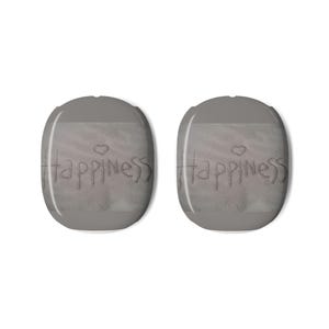 May include: Two gray, oval-shaped objects with the word "happiness" etched into a sandy surface, each with a small heart above the word. The objects have a smooth, rounded top and a slightly darker gray border.
