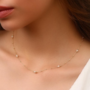 Op de afbeelding: Fijne gouden ketting met kleine parels en kleine gouden kralen. De ketting wordt gedragen en benadrukt het elegante ontwerp. De parels zijn gelijkmatig verdeeld over de ketting, wat een subtiele, verfijnde uitstraling creëert.