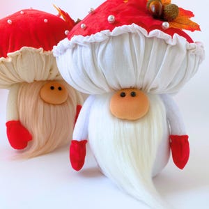 Può includere: Due statuette di gnomi in peluche con grandi cappelli a forma di fungo rosso decorati con perle bianche e foglie autunnali artificiali. Ogni gnomo ha un naso rotondo color pesca, occhi a perla neri, una lunga barba bianca e muffole in tessuto rosso vivo.