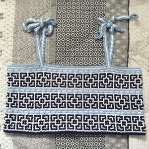 May include: A blue, white, and navy crochet top with a geometric pattern. The top has tie straps and the text "PATTERN ONLY" at the top. The top is made of yarn and is likely handmade.