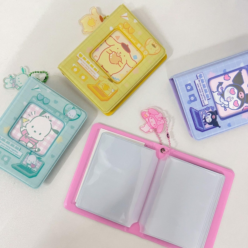 May include: A collection of colorful, small photo albums. The albums are in pastel colors: yellow, blue, and pink. Each album features a different cartoon character on the cover. The pink album is open, revealing clear plastic sleeves for photos.