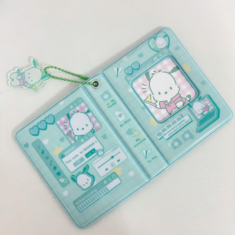May include: A light blue, bi-fold card holder featuring a cartoon dog character. The design includes hearts, stars, and computer-themed graphics. A matching charm hangs from a green chain. The text includes "Too cute to Deleted".