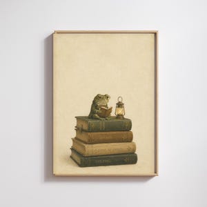 May include: A framed wall art print featuring a frog wearing glasses and a jacket, sitting on a stack of four vintage-style books titled Natural History, Botany, Book of Frogs, and The Pond, accompanied by a small glowing lantern on a cream background.