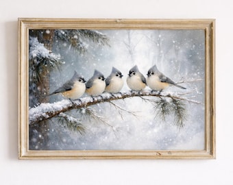 May include: A framed print depicting five small birds perched on a snow-covered branch. The birds have grey and white feathers, set against a snowy, wintery background. The frame is a light brown colour.