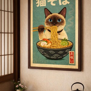 May include: A framed poster featuring a Siamese cat enjoying ramen. The cat, with blue eyes, holds chopsticks above a bowl of noodles, shrimp, and lime. Japanese text is at the top. The poster has a vintage aesthetic with a teal background.