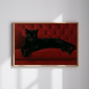 May include: A framed print featuring a black panther with amber eyes, reclining on a tufted red velvet sofa. The panther's sleek black fur contrasts with the rich red of the sofa, creating a striking visual. The artwork is displayed in a wooden frame.