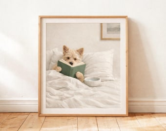 Puede incluir: Una impresión enmarcada muestra un perro pequeño y claro en la cama, leyendo un libro verde. El perro está acurrucado entre almohadas y ropa de cama blancas, con un cuenco pequeño cerca. La obra de arte está en un marco de madera clara, creando una escena doméstica y acogedora.