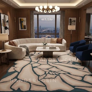 Könnte beinhalten: Ein luxuriöses Wohnzimmer mit einem großen, cremefarbenen Ecksofa, zwei marineblauen Sesseln und einem gemusterten Teppich mit cremefarbenem und türkisfarbenem Design. Ein Marmor-Couchtisch und ein Kronleuchter vervollständigen den Raum. Der Text "HANDSRUGSIN" ist auf dem Teppich zu sehen.