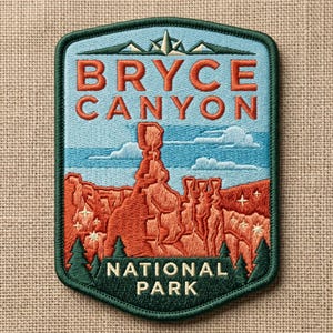 May include: Embroidered patch featuring the words "BRYCE CANYON NATIONAL PARK" in orange and white. The patch depicts a landscape with orange rock formations, blue sky, and green trees. The patch has a green border.
