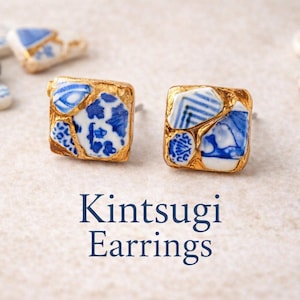 以下が含まれることがあります： 金継ぎの正方形のイヤリング。青と白の磁器の破片が金でセットされています。他の磁器の破片が散らばっています。「Kintsugi Earrings」の文字が下にあります。