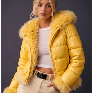 以下が含まれることがあります： 鮮やかな黄色のパファージャケット。フェイクファーの襟と袖口が特徴。光沢のある仕上がりで、黒いベルトが付いています。モデルは白いトップスとクリーム色のパンツを着用。スタイリッシュなアウターウェアです。