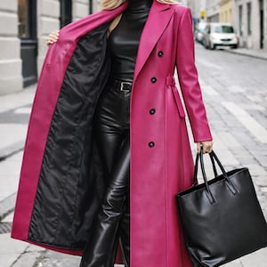以下が含まれることがあります： 黒のタートルネック、革パンツ、ブーツの上に着用された、黒の裏地が付いた長いフクシア色のコート。 黒のトートバッグが手に持たれています。 コートにはベルトと黒いボタンが付いています。