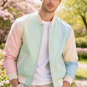 Puede incluir: Chaqueta bomber de colores pastel con paneles rosas, verde menta y azules. La chaqueta tiene cuello, puños y ribetes blancos, y una cremallera plateada. La persona lleva una camiseta blanca y pantalones color caqui. El fondo es un parque con flores rosas.