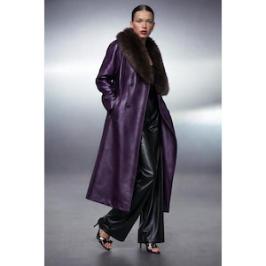 以下が含まれることがあります： 茶色の毛皮の襟が付いた、ダブルブレストの紫色の革のロングコート。 黒いパンツとハイヒールの上にコートを着ています。 コートはクラシックでテーラードデザインです。