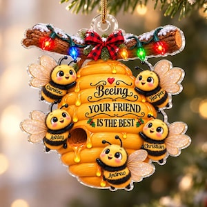 May include: A decorative hanging ornament featuring a yellow beehive with five cartoon bees. Each bee has a name tag: Caroline, Harper, Ashley, Christian, and Andrew. The text reads Beeing YOUR FRIEND IS THE BEST. It includes a branch with colorful lights and a red plaid bow.