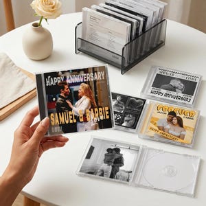 Könnte beinhalten: Eine Sammlung personalisierter CD-Hüllen mit Fotos und Text. Eine Hülle wird in der Hand gehalten und zeigt "HAPPY ANNIVERSARY" und Namen. Andere Hüllen zeigen Paare und die Worte "FOREVER" und "HAPPY ANNIVERSARY". Ein durchsichtiger Kunststoff-Organizer enthält weitere CDs.