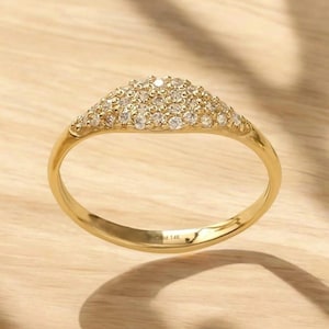 Peut inclure: Une bague en or avec un groupe triangulaire de petits pierres précieuses transparentes. L'anneau est lisse et poli, et les pierres sont serties dans un motif légèrement surélevé. La bague est sur une surface en bois clair.