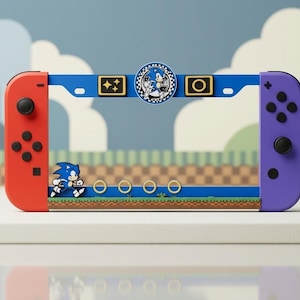 May include: A blue plastic frame designed for a gaming console, featuring a red left controller and a purple right controller. The frame displays a Sonic the Hedgehog graphic with gold rings, a checkered circle emblem, and small rectangular icons.