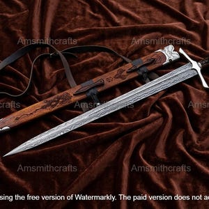May include: A detailed image of a sword with a patterned blade and a wooden sheath. The sword has a silver crossguard and a dark handle. The sheath is brown with carved designs. The sword is approximately 36 inches long.
