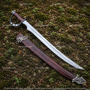 May include: A silver-toned metal sword with a dark red wrapped handle and a curved hand guard. The sword features a long, pointed blade and is accompanied by a matching dark red scabbard with ornate silver-toned metal accents at the tip.